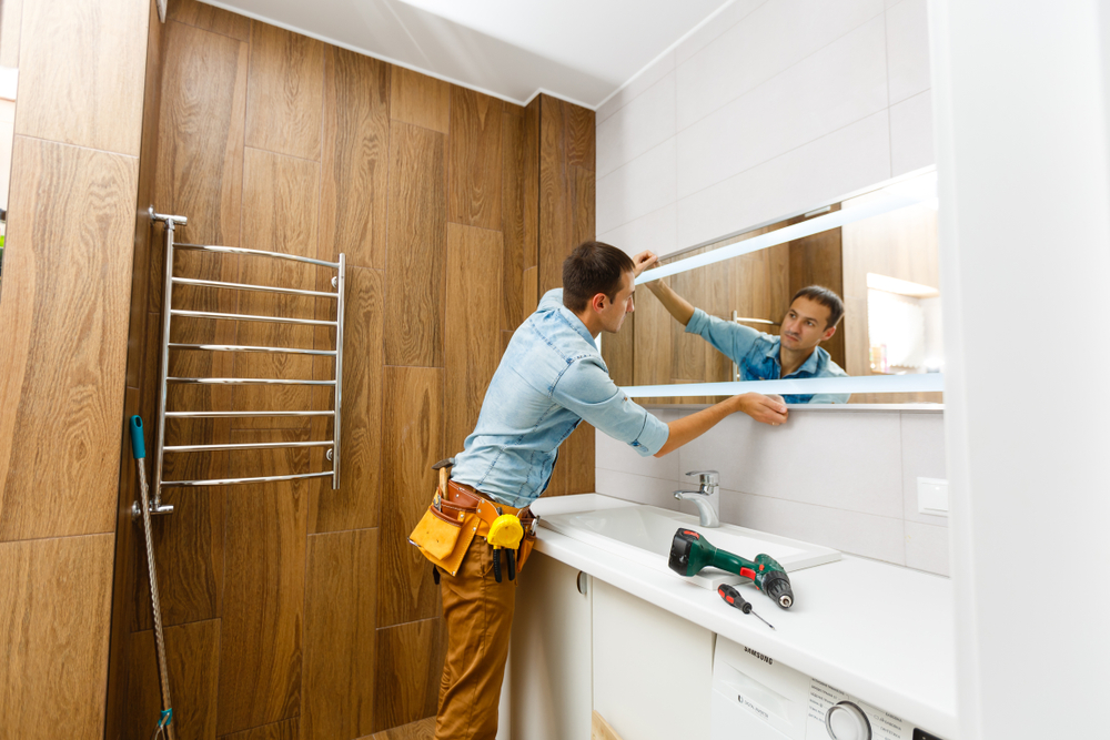 Man,Installing,A,Mirror,On,Wall,In,His,Renewed,Bathroom