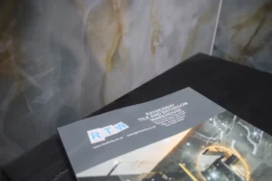 Looking down at a Raynesway Tile & Bathroom Warehouse brochure on top of cabinet and next to a marble tiled wall.
